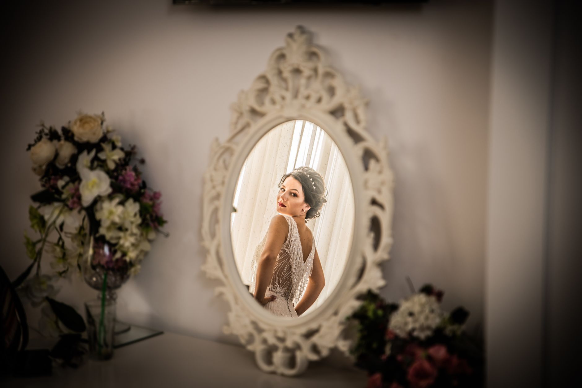 A beautiful bride looks over her shoulder in an elegantly framed mirror reflection, capturing a moment of wedding preparation.