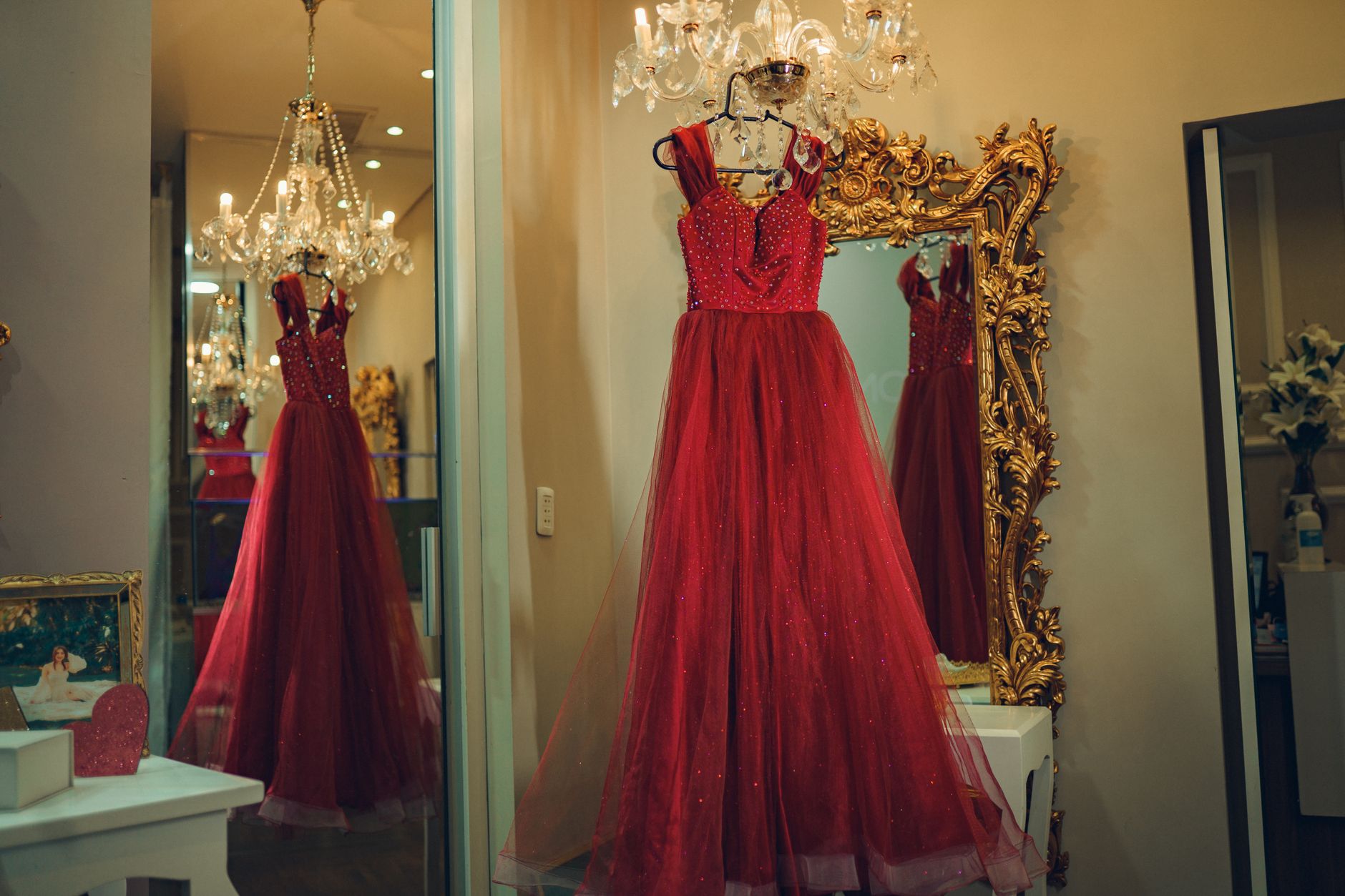 A luxurious red evening gown is reflected in a decorative mirror under a chandelier.
